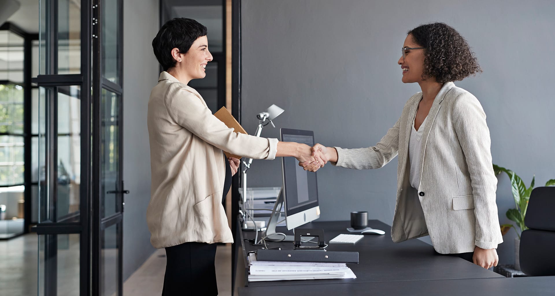 two businesspeople shaking hands over a desk hZQPS