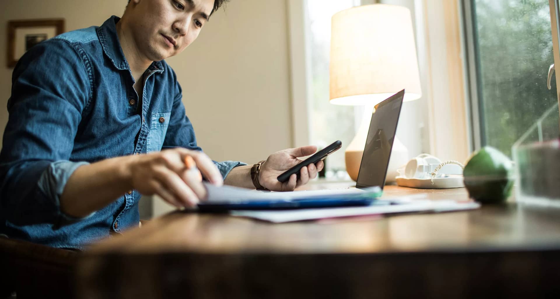 person in home office holding smartphone and looking at document.jpg