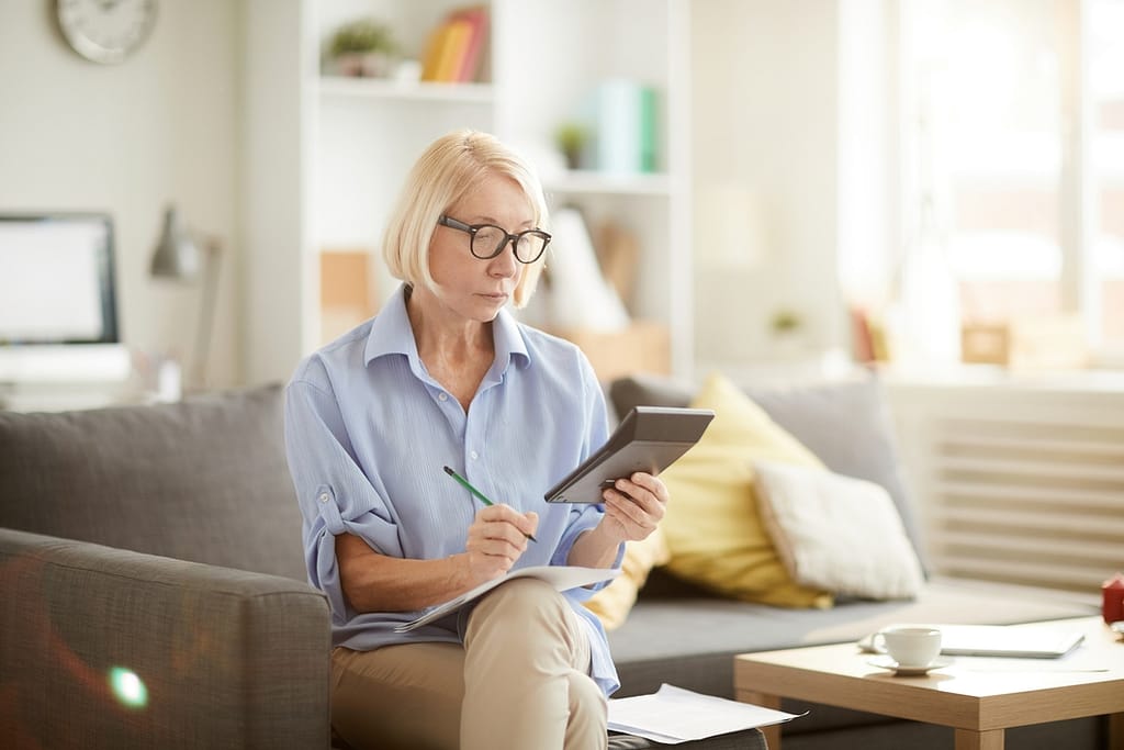older woman sitting on a couch looking at a calculator