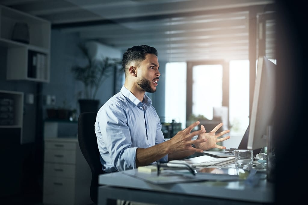 an angry person with hands outstretched looking at a computer monitor