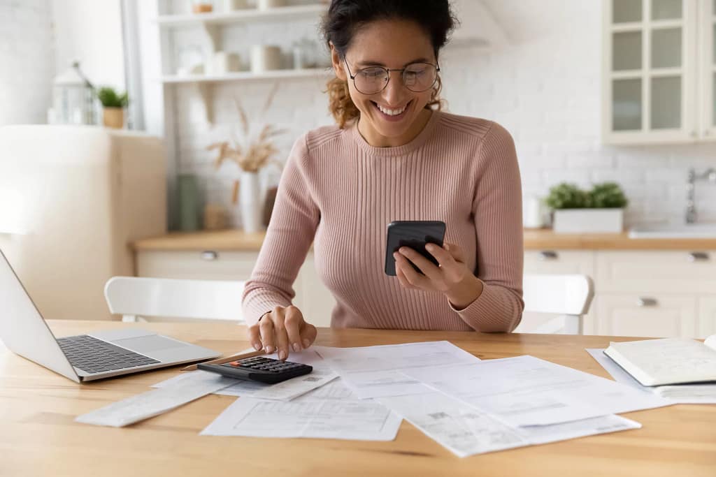 smiling person looking at smartphone and typing on calculator.jpg