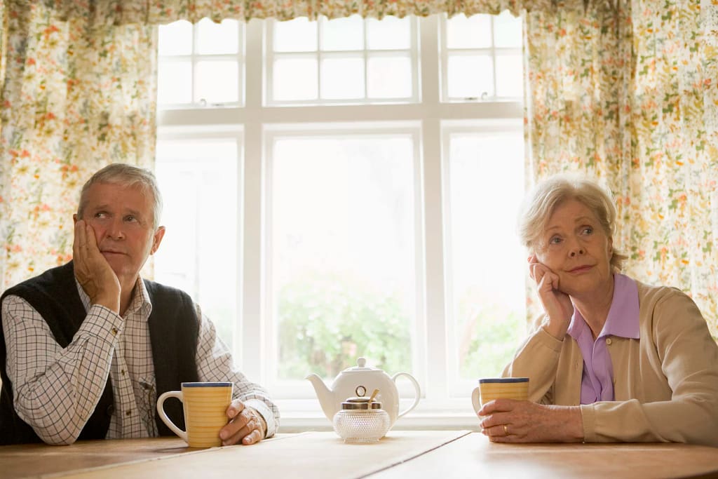 senior man and woman sitting at table resting their faces on their hands looking bored couple retirement.jpg
