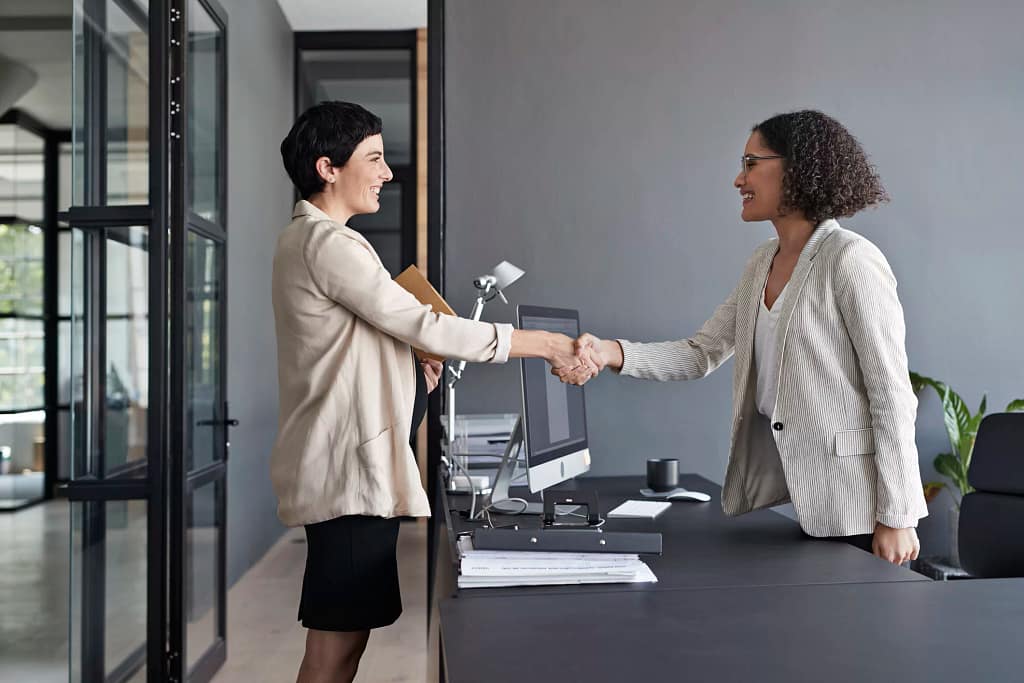 two businesspeople shaking hands over a desk.jpg