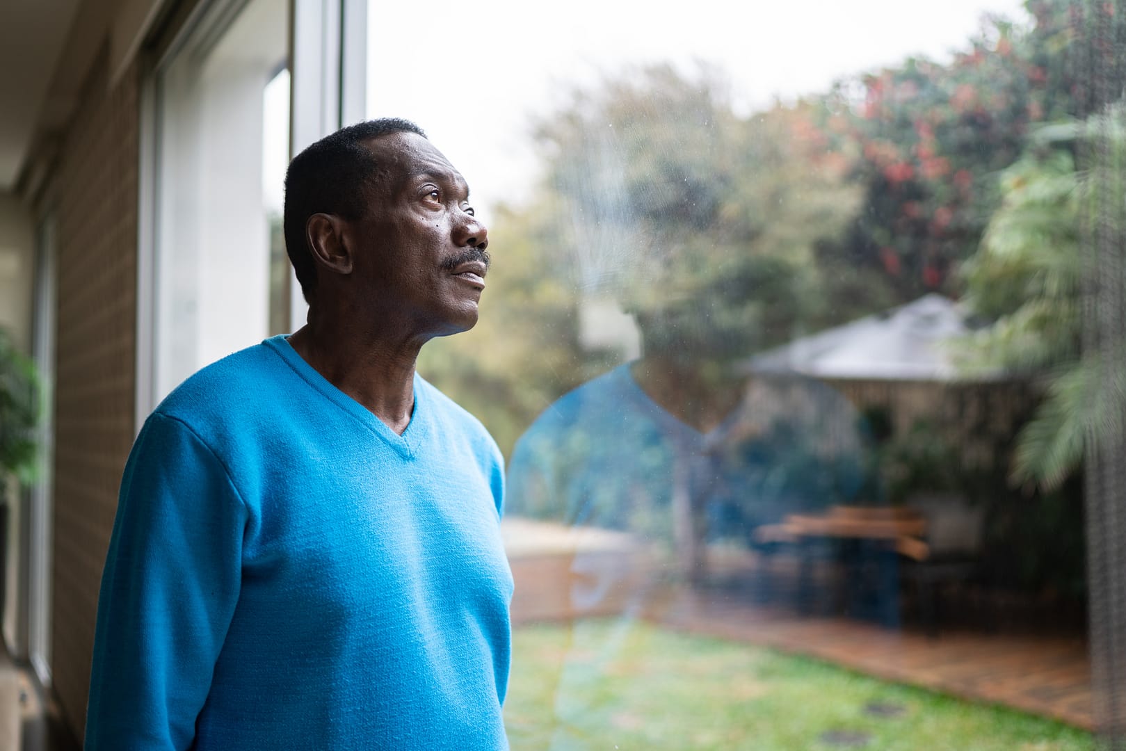 person with serious expression looking out a window