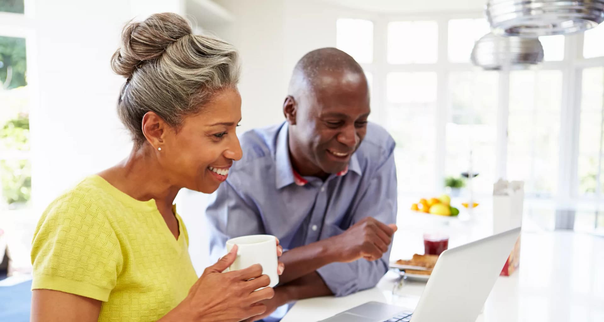 mature man and woman sitting in kitchen looking at laptop computer and smiling couple poc.jpg