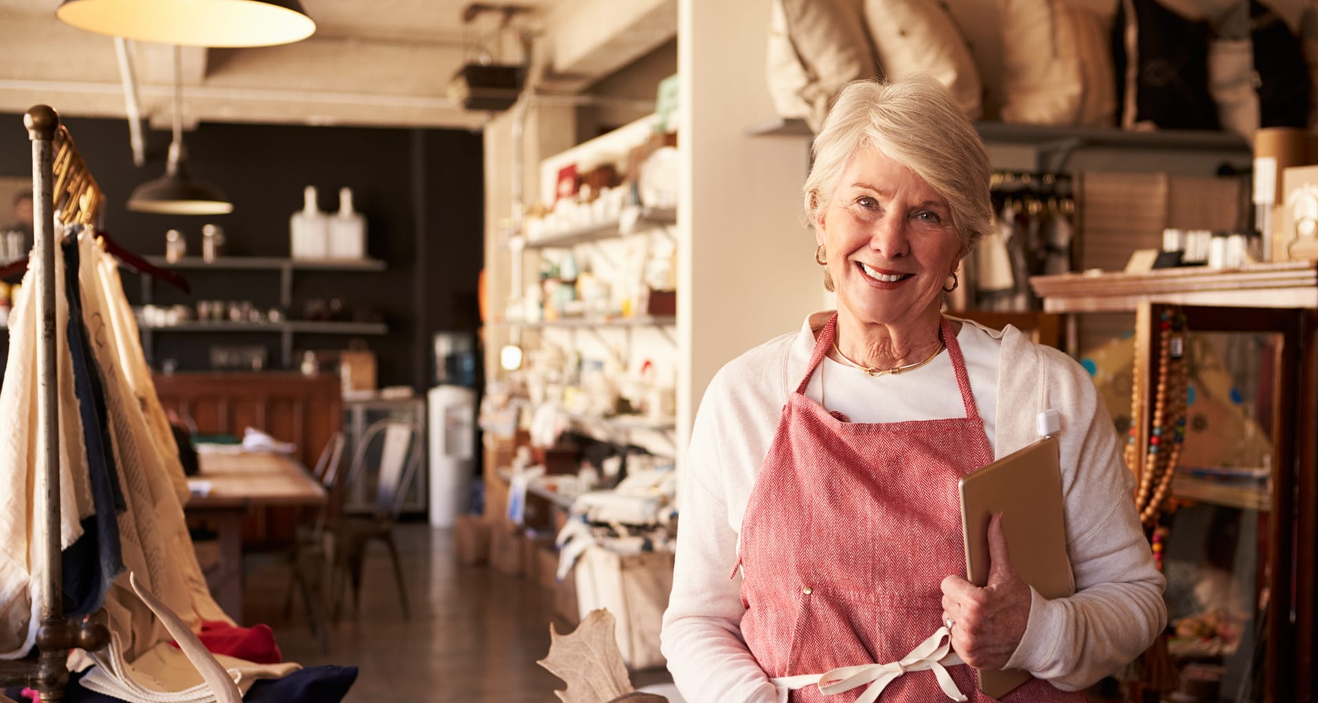 senior woman wearing apron standing next to shelves of apparel in a store small business owner entrepreneur.jpg