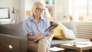 older woman sitting on a couch looking at a calculator