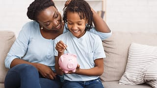 parent and child putting coins into piggy bank at home