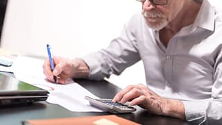 senior taking notes while using calculator gettyimages
