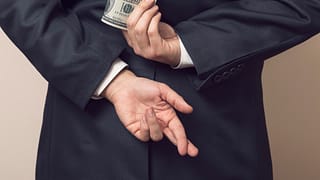 businessman holding cash money bills behind back fingers crossed embezzle getty