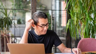 older worker with laptop looking at documents and thinking
