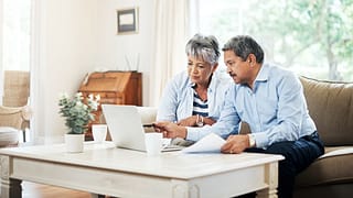 two older people sitting on a couch looking at a laptop copy