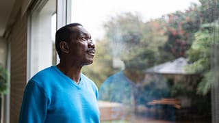 person with serious expression looking out a window