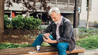 Older gentleman sitting on park bench using h.width Kwa
