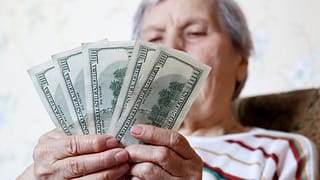 elderly woman retirement social security holding one hundred dollar bills cash getty