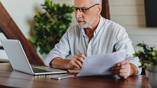 older man laptop holding papers gettyimages