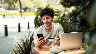 person at outdoor cafe table with laptop phon.width AODczLu.jpg