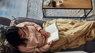 person on couch with blanket and book xRKWoBo.width .jpg