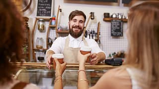 Smiling barista hands coffee to two women PAB.width .jpg