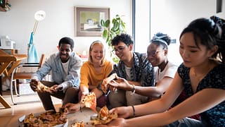 a group of friends eating pizza on an apartme.width DOHqAJ.jpg
