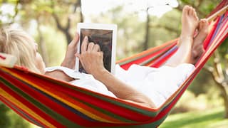 senior woman relaxing in hammock reading ebook.jpg