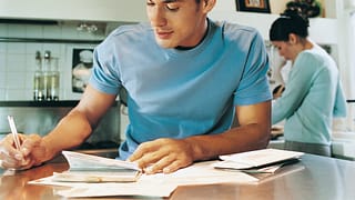 young man sitting at kitchen table writing a .width rpvXbE.jpg