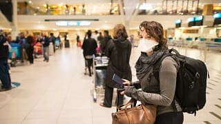 Masked woman with luggage waiting in an airpo.width ogAmB.jpg