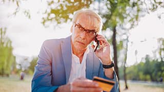older man upset on phone holding credit card.width .jpg