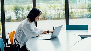 person writing at desk next to laptop DJgfk.width .jpg