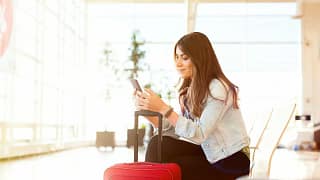 smiling woman with suitcase on phone in airpo.width KCyX.jpg