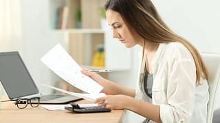woman typing on calculator while looking at d.width qNdigi.jpg