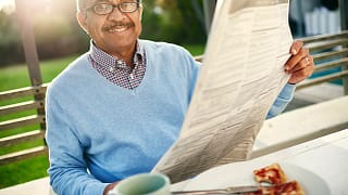 getty smiling person reading newspaper on bench outside.jpg