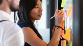 woman in office writing on post its next to m.width VHmiFiK.jpg