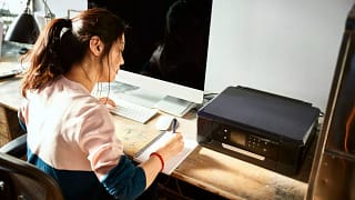 Woman writing in notebook at her home desk U.width .jpg