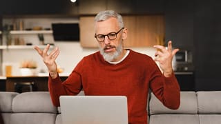 older man at laptop raising his arms as if frustrated.jpg