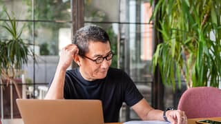 older worker with laptop looking at documents and thinking.jpg