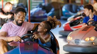 Smiling adult and child riding bumper cars at.width .jpg