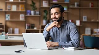 person sitting at a desk looking at a laptop and smiling.jpg