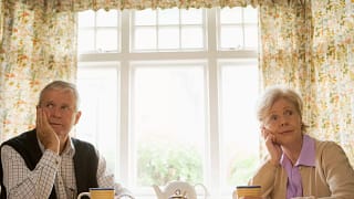 senior man and woman sitting at table resting their faces on their hands looking bored couple retirement.jpg