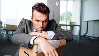 young businessman with desk packed into cardboard box fired from job terminated worker layoff laid off.jpg