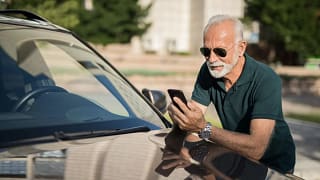 Mature man leans on car looking at phone LCHl.width .jpg