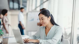 young person sitting at a desk in an office looking at a laptop.jpg