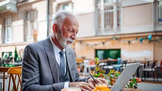 senior businessperson typing on laptop at coffee shop.jpg