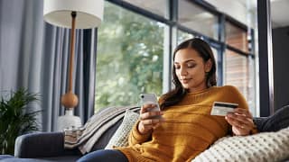 Woman on couch holding phone and credit card .width cWRJtw.jpg
