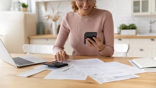smiling person looking at smartphone and typing on calculator.jpg