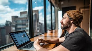 person sitting in front of laptop looking out window of office building.jpg