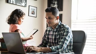 person sitting at a desk looking at a laptop with a child nearby.jpg