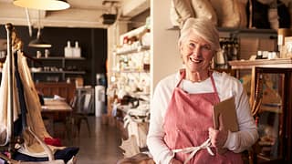 senior woman wearing apron standing next to shelves of apparel in a store small business owner entrepreneur.jpg