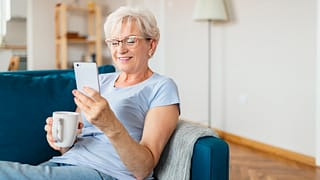 smiling senior holding coffee mug and looking at smartphone.jpg