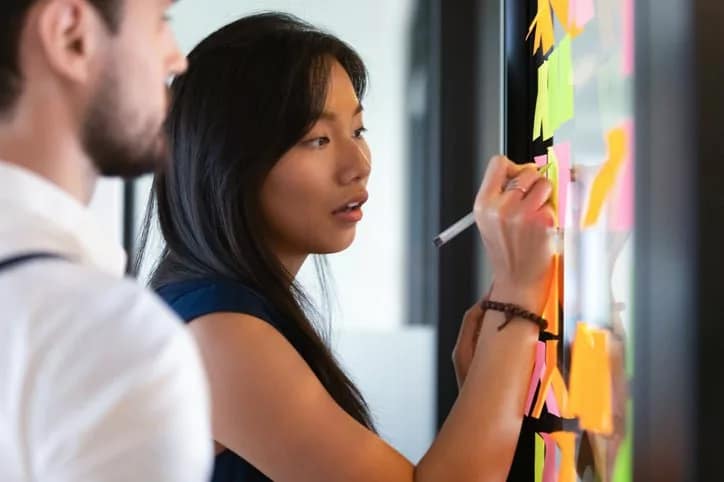 woman in office writing on post its next to m.width VHmiFiK.jpg